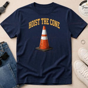 May include: Navy blue t-shirt featuring a graphic of an orange and white traffic cone on a black base. The text "HOIST THE CONE" is arched above the cone in yellow. A casual tee for everyday wear.