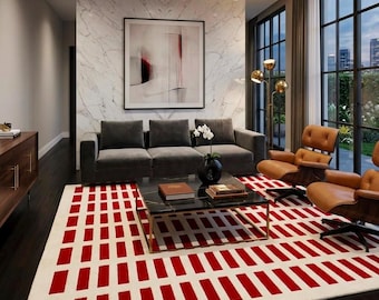 May include: A large rectangular area rug featuring a repeating pattern of bold red vertical rectangles set against a cream-colored background, covering the floor beneath a black marble coffee table, a gray sofa, and two tan leather lounge chairs.
