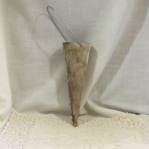 Puede incluir: Un jarrón de pared en forma de cono hecho a mano con madera natural. Presenta una superficie rugosa y texturizada y un asa de alambre metálico para colgarlo. El jarrón se muestra sobre un fondo blanco.