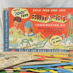 May include: Vintage Bild-A-Set Constructor Kit box with the text "Build Your Own Toys" and "Makes 1001 Toys." The box features illustrations of children and toy structures. The kit includes wooden pieces and instructions.
