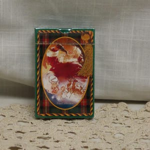 May include: A green rectangular box with a plaid pattern border. The box features an oval image of Santa Claus, reindeer, and a clock. The text "Travel Refresh" is below the image. A gold tassel hangs from the top right corner.