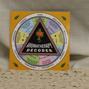 May include: A square yellow Aromatherapy Decoder chart featuring a central black triangle with an orange flower graphic. The chart is divided into segments labeled with essential oils like Basil, Bergamot, and Black Pepper, each listing health benefits.