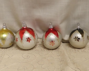 May include: Four vintage Christmas ornaments. The ornaments are round, with silver bases and various designs in gold, red, and black. Each ornament has a metal cap for hanging.