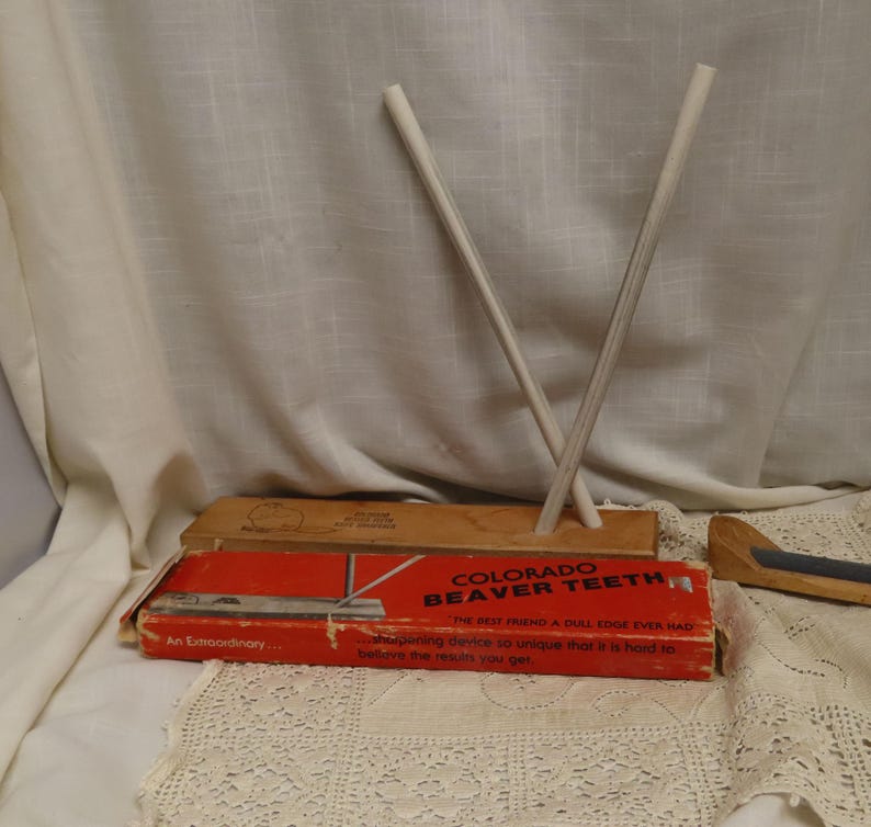 May include: An image of a vintage Colorado Beaver Teeth sharpening device. The red and orange box has text that reads "COLORADO BEAVER TEETH" and "THE BEST FRIEND A DULL EDGE EVER HAD". Two white sharpening rods are crossed.