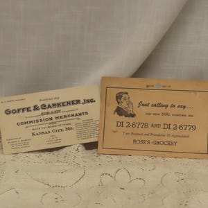 May include: Two vintage business cards. One card reads "GOFFE & CARKENER, INC. GRAIN COMMISSION MERCHANTS" and the other card says "Just calling to say... DI 2-6778 AND DI 2-6779 ROSE'S GROCERY". The cards are on a white lace surface.