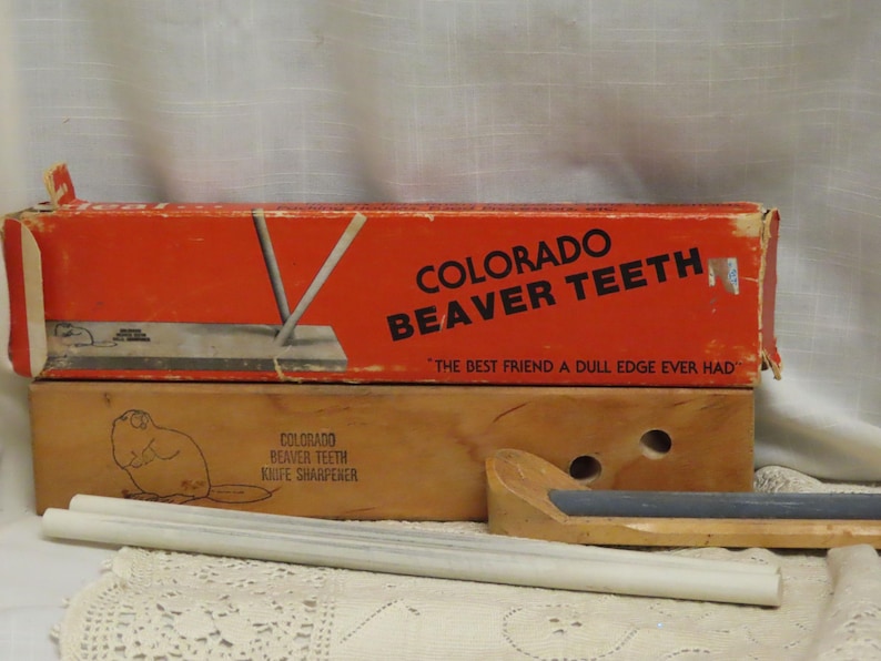 May include: Vintage Colorado Beaver Teeth knife sharpener set. The set includes a red and brown box with the text "COLORADO BEAVER TEETH" and "THE BEST FRIEND A DULL EDGE EVER HAD". The set also includes sharpening rods and a wooden sharpening tool.