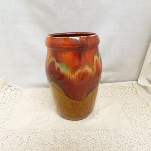 Könnte beinhalten: Eine glasierte Keramikvase mit breiter Öffnung und rundem Körper. Die Vase weist eine Mischung aus Farben auf, darunter Brauntöne, Orange und Grün. Die Vase ist ein dekorativer Gegenstand.