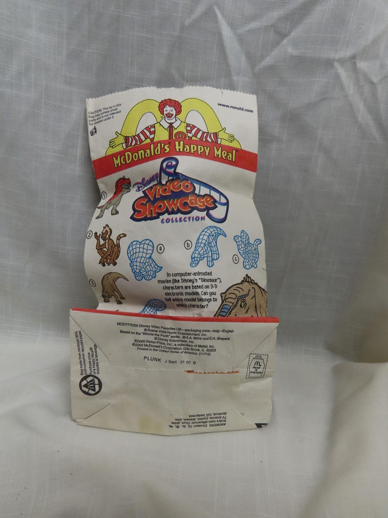 May include: A white paper bag with a McDonald's Happy Meal logo and a Disney Video Showcase Collection logo. The bag features a cartoon image of Ronald McDonald and a variety of animated characters from Disney's Dinosaur movie. The text on the bag reads "In computer-animated movies like Disney's "Dinosaur" characters are based on 3-D electronic models. Can you tell which model belongs to which character?"