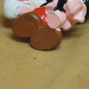 Puede incluir: Primer plano de la parte inferior de una figura de Mickey Mouse. Los pies de la figura son marrones, con el texto "&copy; THE WALT DISNEY CO. MADE IN CHINA" impreso en la parte inferior. Se ven los pies rosas y los zapatos negros de la figura.