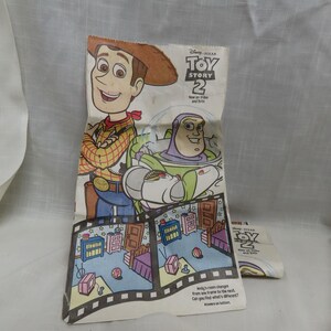 May include: A white paper bag with a fold-out design featuring Woody and Buzz Lightyear from the movie Toy Story 2. The bag has a spot-the-difference game with two images of Andy's room. The text on the bag reads "Disney Pixar Toy Story 2 New on Video and DVD".