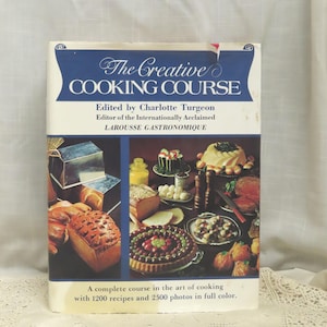 May include: A vintage cookbook titled "The Creative Cooking Course" with a blue banner and images of food. The cover features text, including the editor's name and the phrase "LAROUSSE GASTRONOMIQUE." The book promises 1200 recipes and 2500 photos.