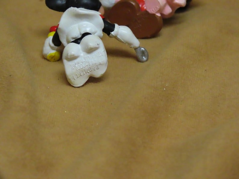 Puede incluir: Primer plano de una figura de Mickey Mouse tumbada boca arriba. La figura es principalmente blanca, con pantalones cortos negros, zapatos amarillos y guantes rojos. Las palabras "MADE IN HONG KONG" son visibles en el pie de la figura.