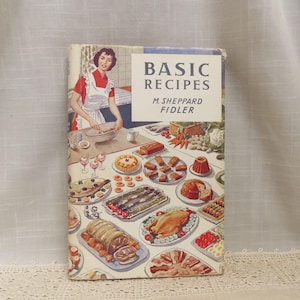 Può includere: Libro di cucina vintage intitolato "Basic Recipes" di M. Sheppard Fidler. La copertina presenta una donna con una maglia rossa e un grembiule bianco, che cucina. Vari piatti sono illustrati sulla copertina, tra cui un pollo arrosto, torte e altri pasti cotti.