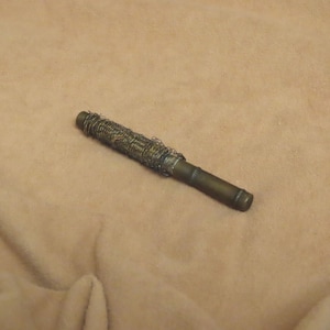 May include: A vintage-style, cylindrical object with a brass-colored body and a wire-wrapped section. The object is lying on a tan fabric surface. The wire wrapping appears to be made of a dark, possibly oxidized metal.