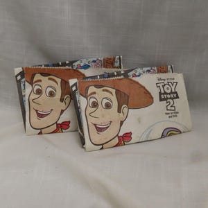 May include: Two white cardboard lunch bags with a Toy Story 2 theme. The bags feature a cartoon image of Woody from the movie. The text on the bag reads "Disney Pixar Toy Story 2 Now on Video and DVD".