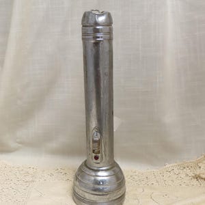 Könnte beinhalten: Eine vintage silberne Taschenlampe mit einem roten Knopf und einem Schalter an der Seite.