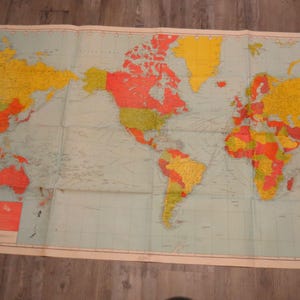 Puede incluir: Un mapa del mundo vintage con un fondo oceánico azul claro y países en tonos de rojo, amarillo y verde. El mapa es rectangular y tiene un borde color crema. Una pequeña caja roja y blanca con texto está en la esquina inferior izquierda.