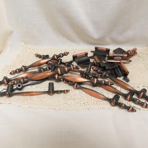 May include: A collection of antique bronze-colored cabinet hardware, including handles and hinges. The handles have a decorative, turned design with a copper finish. The hardware is arranged on a cream-colored lace doily.
