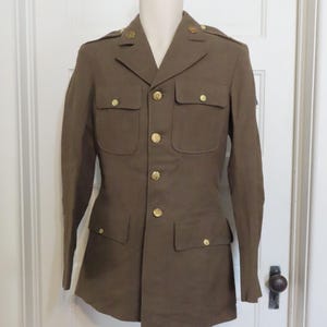May include: A brown military uniform jacket with gold buttons and insignia. The jacket has a collared neckline, long sleeves, and two flap pockets on the front.