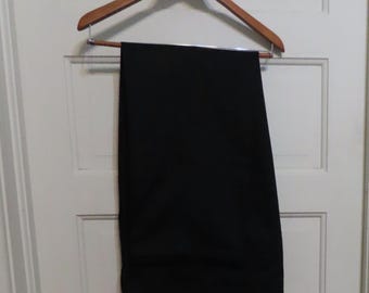 May include: Black dress pants hanging on a wooden hanger. The pants are a solid black color and appear to be made of a smooth fabric. The hanger is a light brown color and is hanging on a white door.
