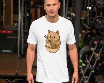 Puede incluir: Camiseta blanca de manga corta con un diseño de gato de dibujos animados comiendo ramen. El gato marrón y esponjoso usa palillos para comer fideos, huevo y verduras de un cuenco de ramen.