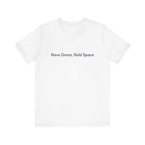 Könnte beinhalten: Ein weißes T-Shirt mit dem dunkelblauen Aufdruck "Have Grace, Hold Space". Das T-Shirt hat einen Rundhalsausschnitt, kurze Ärmel und ist aus weichem Stoff gefertigt.