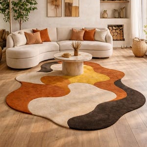 May include: A contemporary living room with a cream-coloured curved sofa and orange cushions. An abstract rug in brown, orange, yellow, and cream tones lies on the wooden floor. A woven pendant light hangs above a marble coffee table. The rug measures approximately 200cm x 300cm.