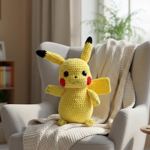 Peut inclure: Une poupée Pikachu jaune au crochet, avec des oreilles à bout noir, des joues rouges et des yeux noirs. La peluche est assise sur une couverture crème drapée sur un fauteuil gris. Les bras de la poupée sont tendus et ses ailes sont visibles.