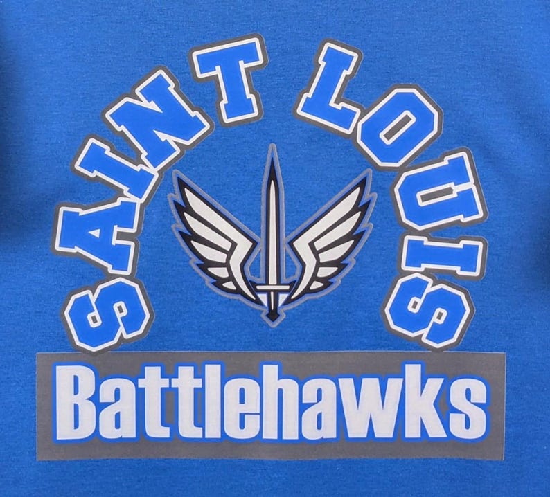 May include: A blue graphic design featuring the words "Saint Louis" in a curved, white-outlined font above the word "Battlehawks" in a rectangular banner. A sword and wing emblem is centered.