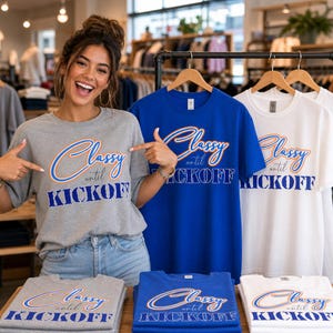 May include: A display of t-shirts in gray, blue, and white, each featuring the text "Classy until Kickoff" in a stylized font. The shirts are on hangers and folded on a table. A person is pointing at the shirts.