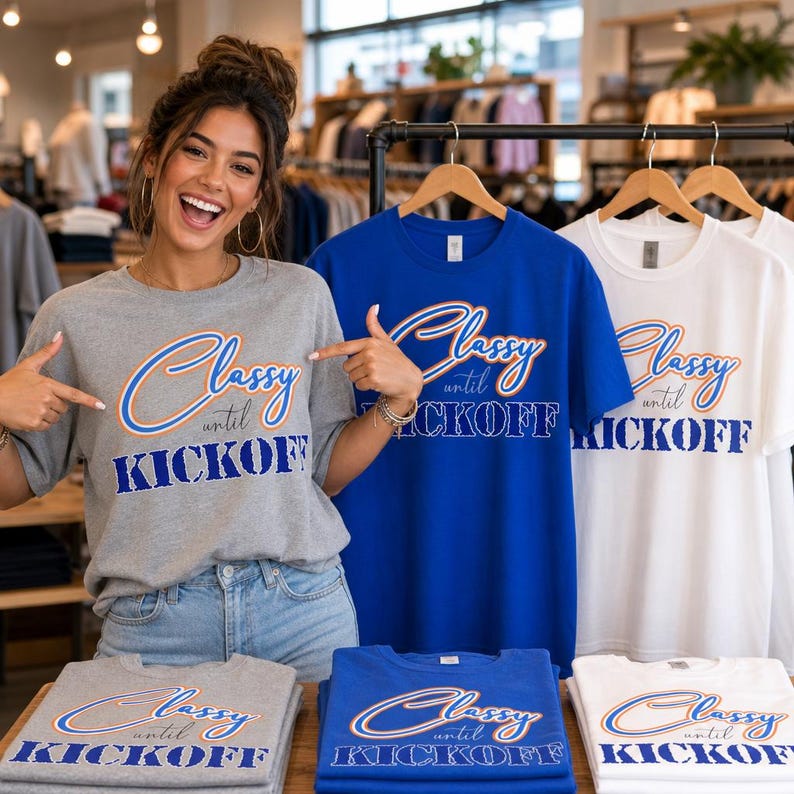 May include: A display of t-shirts in gray, blue, and white, each featuring the text "Classy until Kickoff" in a stylized font. The shirts are on hangers and folded on a table. A person is pointing at the shirts.