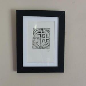 May include: A black framed print featuring a square black and white abstract graphic design with curved lines. The artwork includes the handwritten text 1/7 on the bottom left and SAME 1/24 on the bottom right, set against a white mat board.