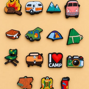 May include: A collection of fourteen colourful rubber shoe charms featuring camping-themed designs including a campfire, camper van, mountains, s'mores, tent, camera, backpack, water bottle, and a sign that reads TAKE A HIKE and I LOVE CAMP.