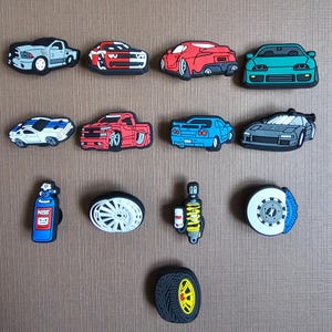May include: A collection of thirteen rubber shoe charms featuring various sports cars, a pickup truck, a blue nitrous oxide bottle with the text NOS, a white wheel rim, a yellow suspension coil, a brake disc with a blue caliper, and a black tire.