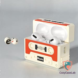 Puede incluir: Una funda blanca y naranja con forma de cinta de cassette con auriculares blancos. La funda tiene la palabra "Music" impresa. Los auriculares son blancos con detalles en negro. La funda está abierta, revelando los auriculares en su interior.