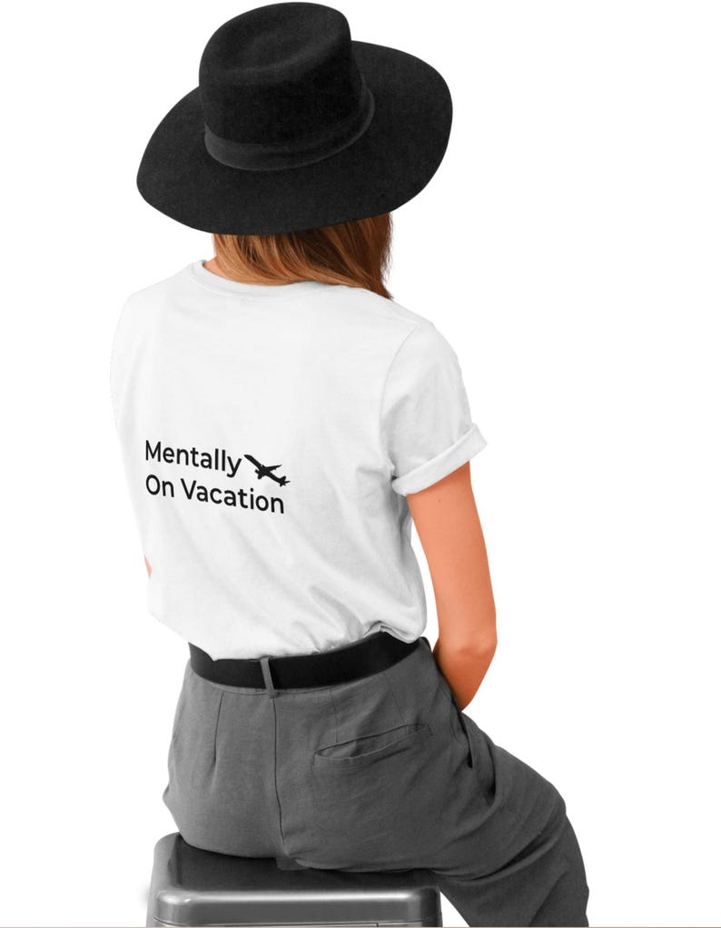 以下が含まれることがあります： 黒い帽子、白いTシャツ、グレーのズボンを着用した人。白いTシャツには「Mentally On Vacation」の文字と小さな飛行機のグラフィックが入っています。その人はスツールに座っています。
