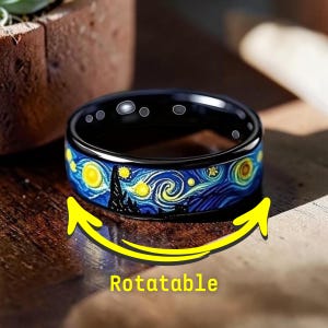 Può includere: Anello nero con un design a notte stellata blu e giallo. L'anello è girevole e presenta un design simile a un dipinto. L'anello è su una superficie di legno.