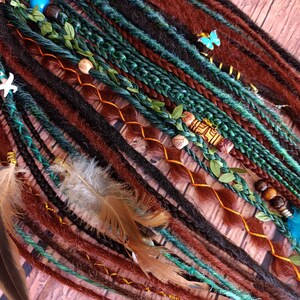 May include: A set of synthetic dreadlocks in shades of brown, dark green, and teal. The hair extensions feature braided sections, green leaf accents, wooden beads, a small blue butterfly charm, a white starfish charm, and brown feathers.