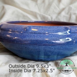 May include: A blue ceramic bonsai pot with a textured surface and a contrasting orange interior. The pot has an outside diameter of 9.5x3 inches and an inside diameter of 7.25x2.5 inches. The text "Bonsai of Gresham" is visible.