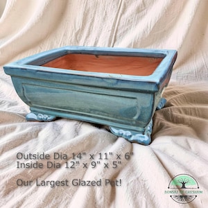 May include: A square, glazed bonsai pot in a teal blue color. The pot has decorative feet and a rectangular shape. Outside dimensions are 14" x 11" x 6", inside dimensions are 12" x 9" x 5". The text reads "Our Largest Glazed Pot!"