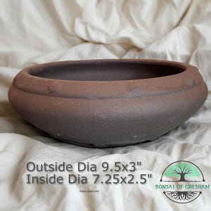 May include: A brown, oval-shaped bonsai pot with a textured surface. The outside diameter is 9.5 inches by 3 inches, and the inside diameter is 7.25 inches by 2.5 inches. The pot has a simple, elegant design, suitable for bonsai trees.