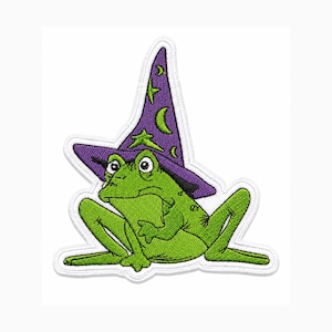 May include: An embroidered patch featuring a bright green frog wearing a pointed purple hat decorated with yellow stars and crescent moons. The frog is depicted in a seated position with its legs tucked, outlined by a white border.