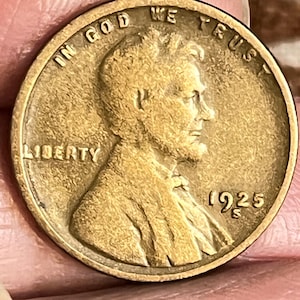 May include: A vintage bronze coin featuring a profile of a man, with the words "IN GOD WE TRUST" and "LIBERTY" inscribed. The year "1925" is visible. The coin has a worn, aged appearance.