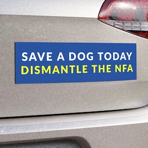 May include: A blue rectangular bumper sticker with white text that reads "SAVE A DOG TODAY" and yellow text that reads "DISMANTLE THE NFA". The sticker is affixed to the back of a silver car.