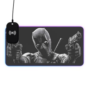 May include: Black and white mousepad featuring Deadpool holding two guns. The design includes a wireless charging pad with a wireless symbol. The mousepad has a black background with a colorful border.