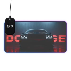 May include: Black rectangular mouse pad featuring a Dodge Challenger car graphic. The car is centered with bright headlights and the word "DODGE" in red. A black wireless charging pad is attached to the mouse pad.