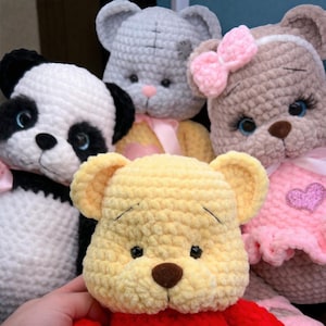 Op de afbeelding: Een verzameling handgemaakte gehaakte knuffels, waaronder een panda, een grijze beer, een Winnie de Poeh beer en een bruine beer met een roze strik. De knuffels zijn zacht en pluche, met gedetailleerde kenmerken.
