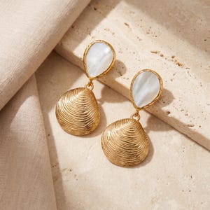 Peut inclure: Une paire de boucles d'oreilles pendantes composées d'un pendentif en métal doré en forme de coquillage avec des stries horizontales, suspendu à une nacre blanche en forme de goutte sertie dans une monture en métal doré avec fermoir.