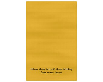 May include: Mustard yellow kitchen towel with the text "Where there is a will there is Whey Just make cheese" in a black, simple font. The towel has a textured surface.