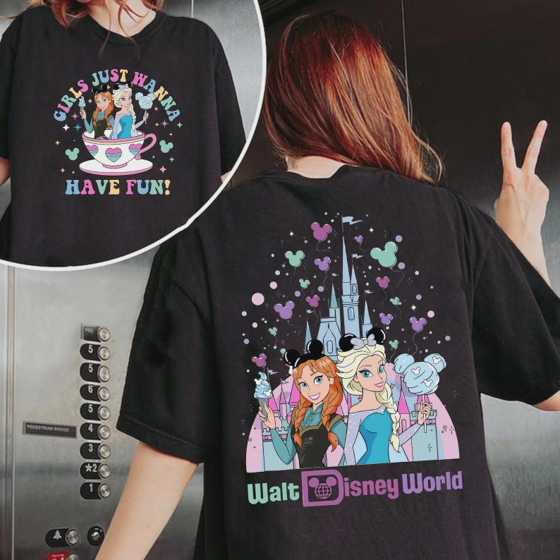 May include: Black t-shirt with a colorful graphic featuring Anna and Elsa from Frozen, holding treats in front of a castle, with "Walt Disney World" text. The front has the text "Girls Just Wanna Have Fun!"